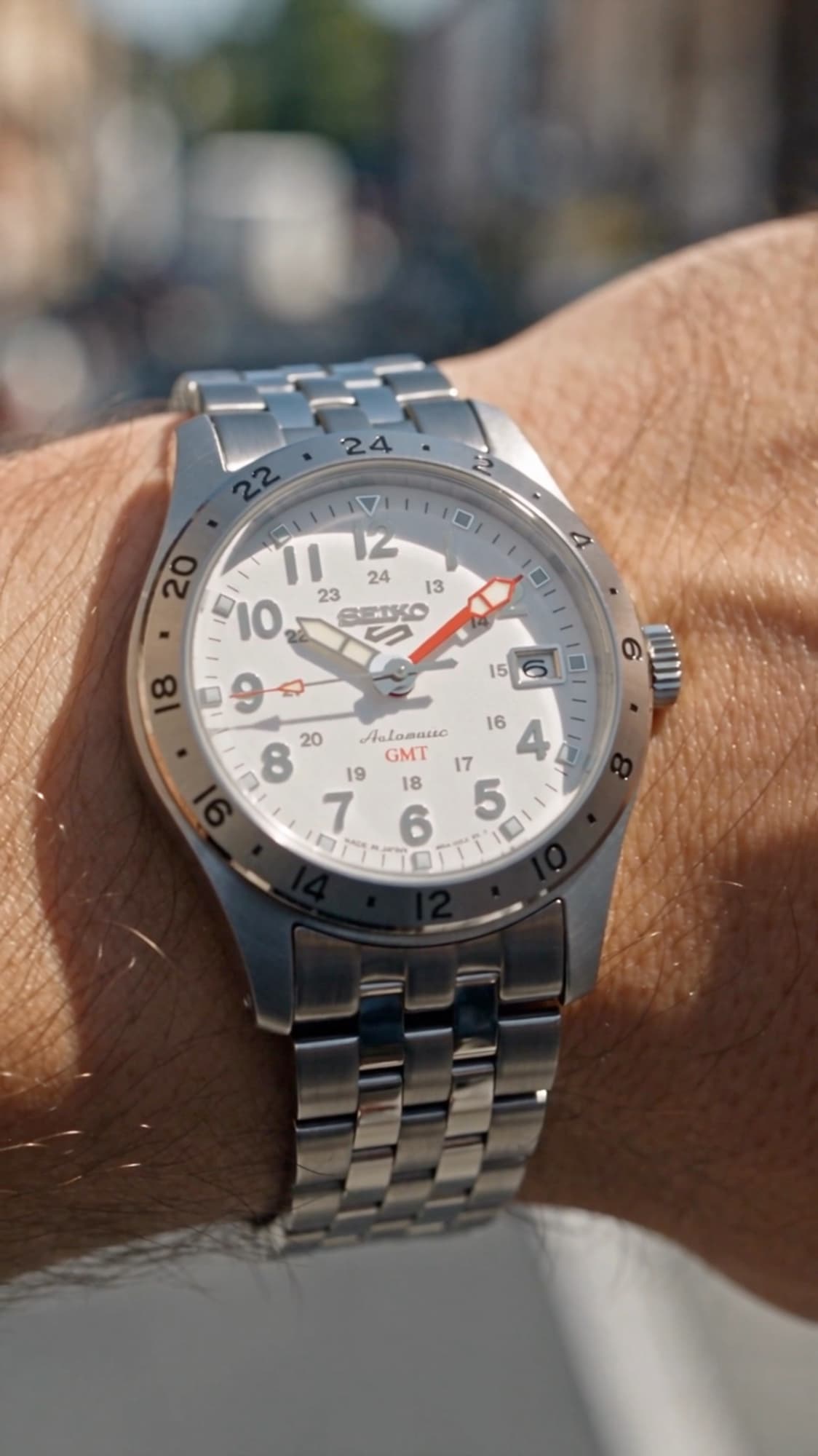 The finished Seiko 5 Sports GMT on a real wrist, steel bracelet catching the light on a bright street