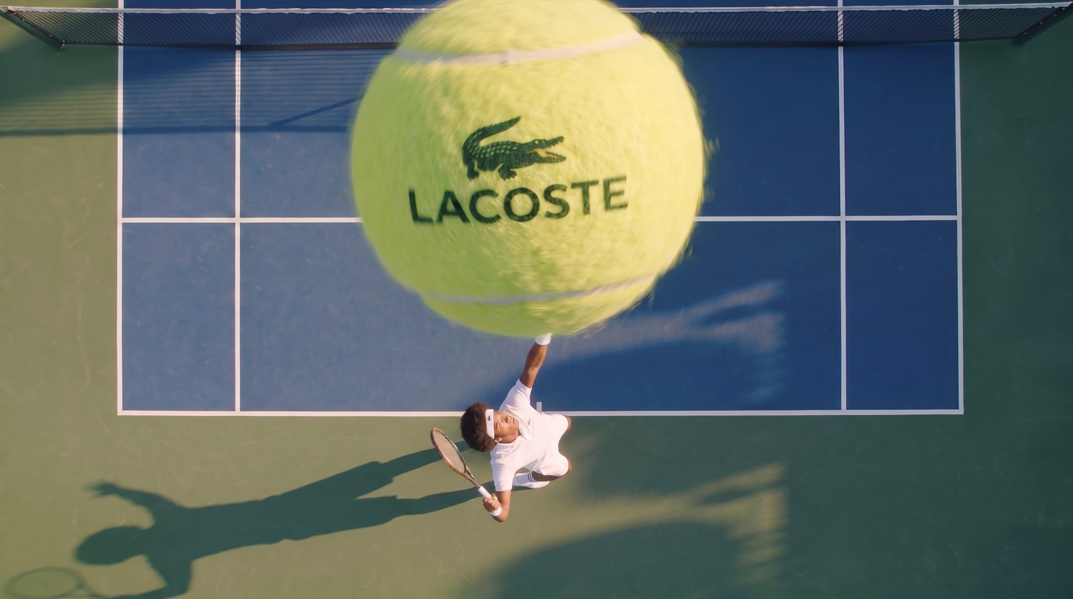Overhead shot of a player mid-serve beneath an oversized crested tennis ball