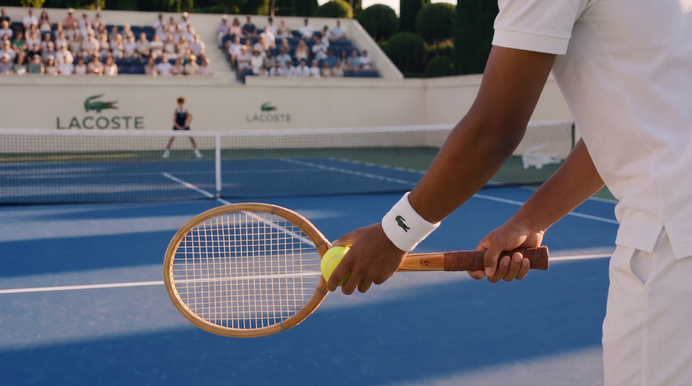 Close-up of a wooden racquet and ball held at the baseline, crest on the wristband